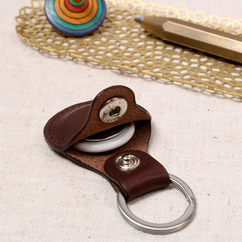 Offener AirTag Anhänger aus pflanzlich gegerbtem Leder in Chocolate von Good Wilhelm mit eingelegtem Apple AirTag, Edelstahl-Schlüsselring, liegend auf einem Holztisch