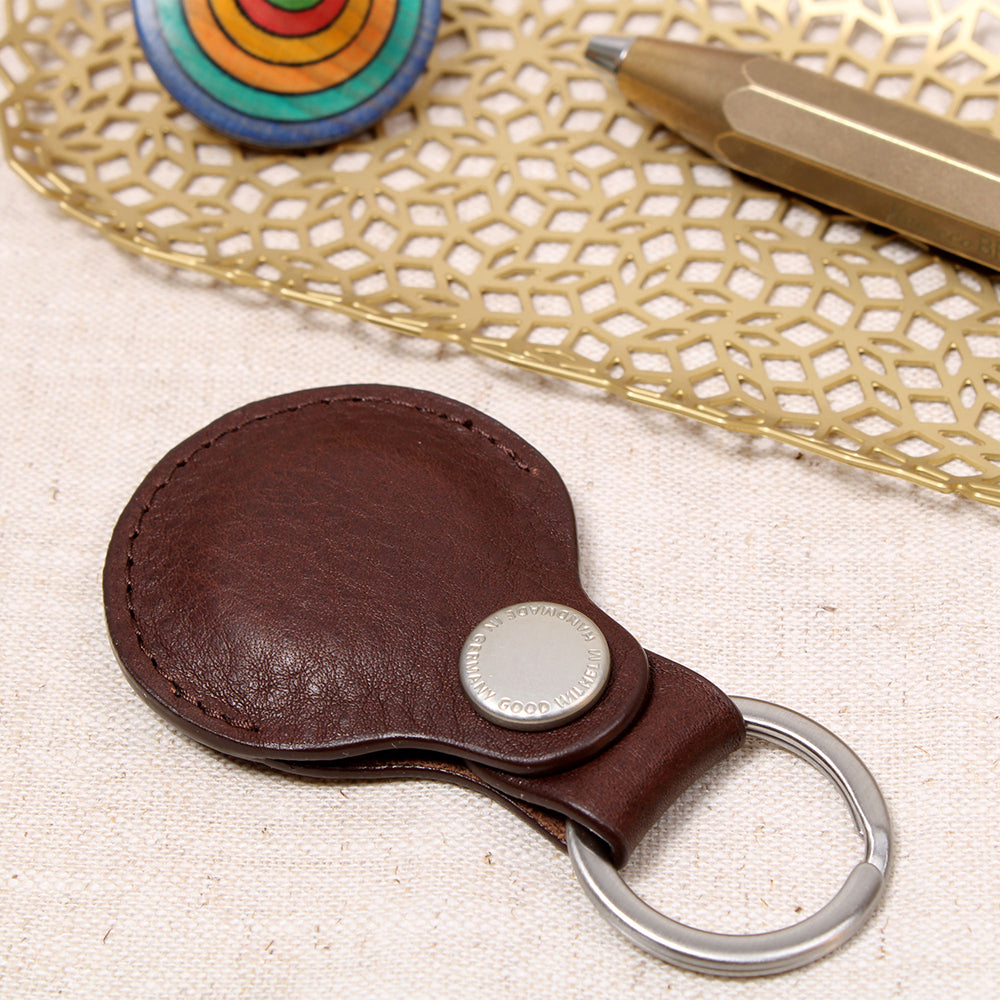 Geschlossener AirTag Anhänger aus pflanzlich gegerbtem Leder in Chocolate mit Prym-Druckknopf und Edelstahl-Schlüsselring von Good Wilhelm – liegend auf einem Tisch