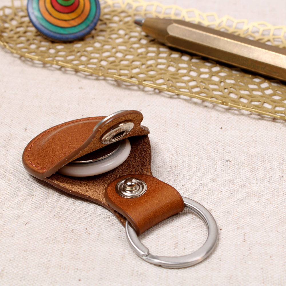 Offener AirTag Anhänger aus pflanzlich gegerbtem Leder in Cognac von Good Wilhelm mit eingelegtem Apple AirTag, Edelstahl-Schlüsselring, liegend auf einem Holztisch