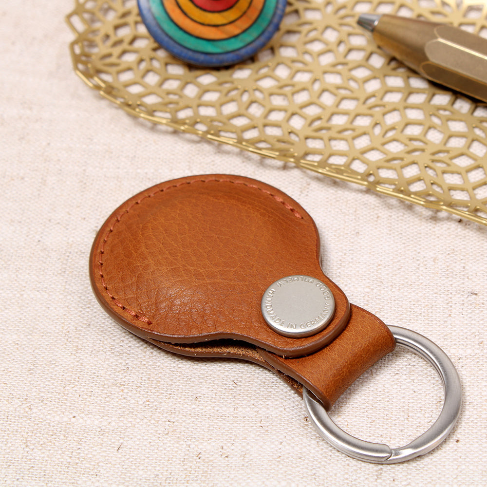 Geschlossener AirTag Anhänger aus pflanzlich gegerbtem Leder in Cognac mit Prym-Druckknopf und Edelstahl-Schlüsselring von Good Wilhelm – liegend auf einem Tisch