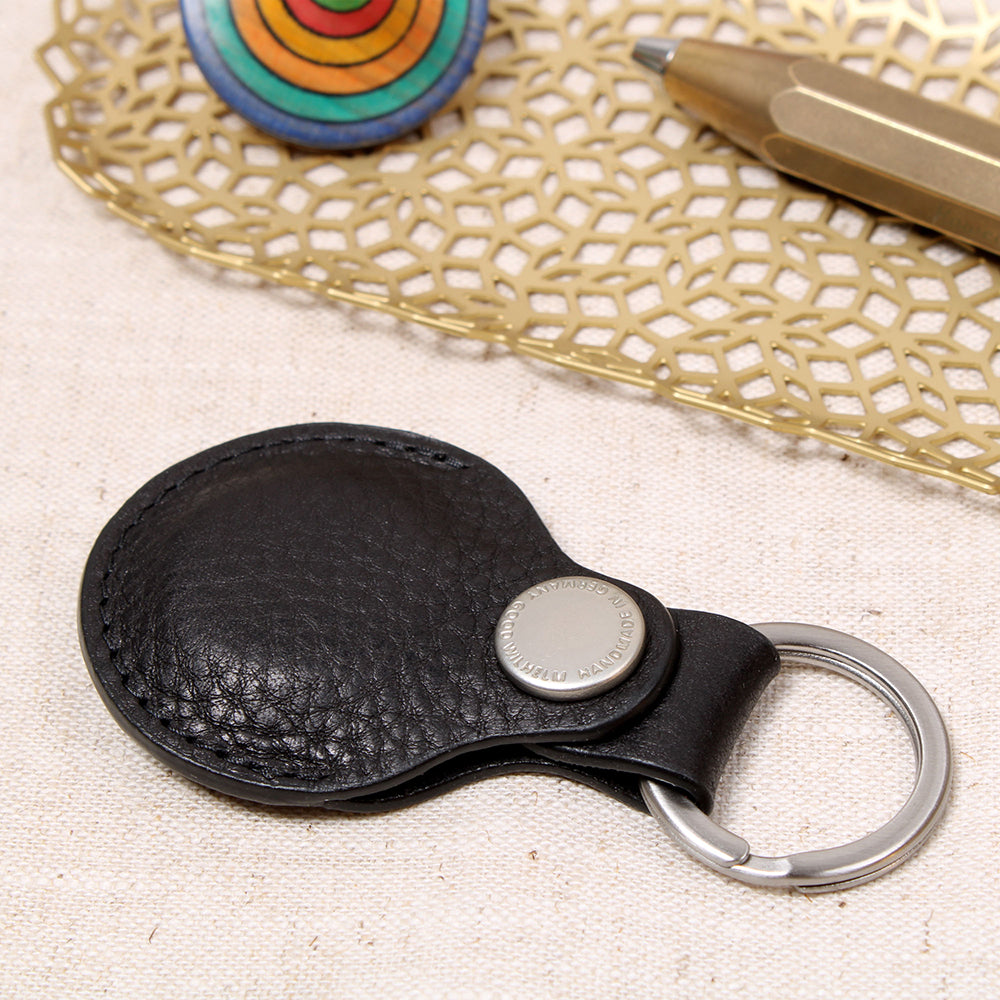 Geschlossener AirTag Anhänger aus pflanzlich gegerbtem Leder in Schwarz mit Prym-Druckknopf und Edelstahl-Schlüsselring von Good Wilhelm – liegend auf einem Tisch