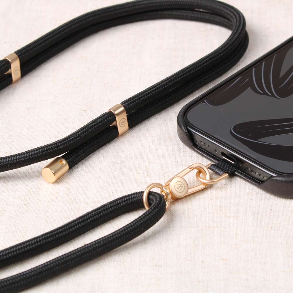 Good Wilhelm Handykette Handyband schwarz mit goldenem Karabiner, liegt auf Tisch