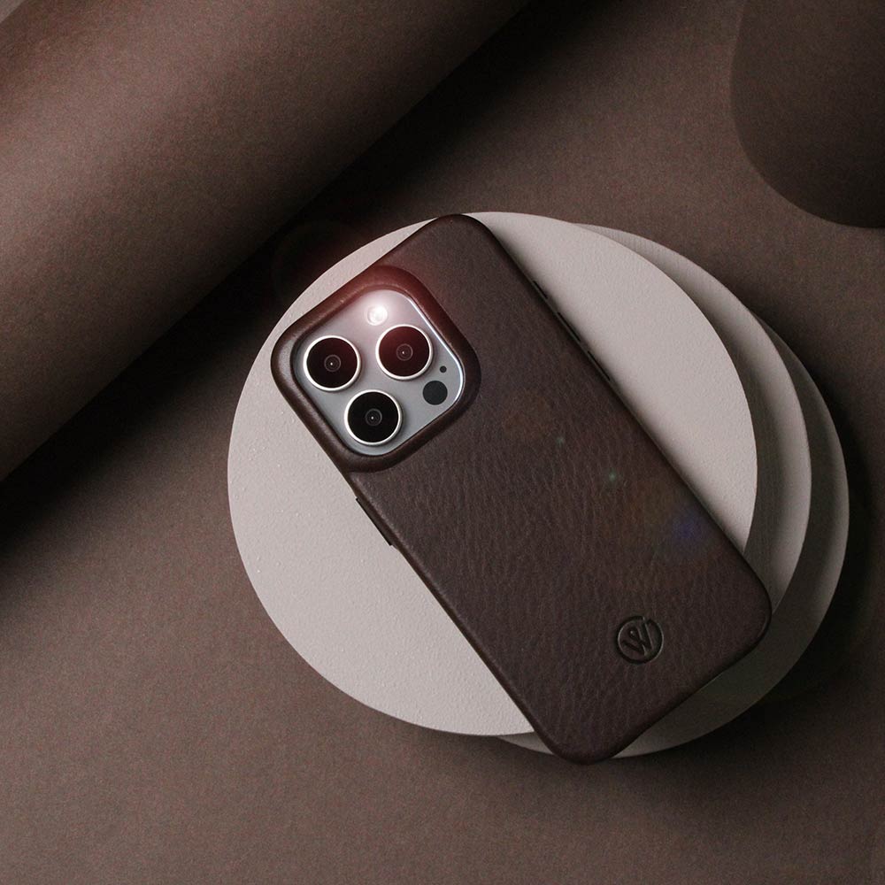 Dunkelbraune iPhone-Hülle aus hochwertigem Leder, liegend auf einem Tisch mit dekorativen Holzscheiben