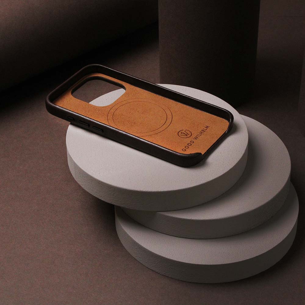 Braune iPhone-Hülle aus hochwertigem Leder, liegend auf einem Tisch mit dekorativen Holzscheibendarunter