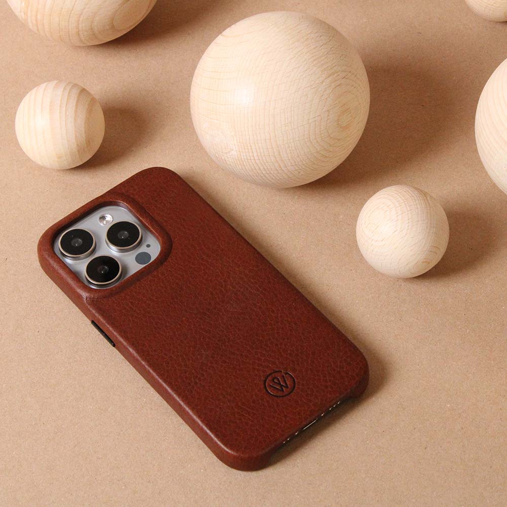 Braune iPhone-Hülle aus hochwertigem Leder, liegend auf einem Tisch mit dekorativen Holzkugeln im Hintergrund