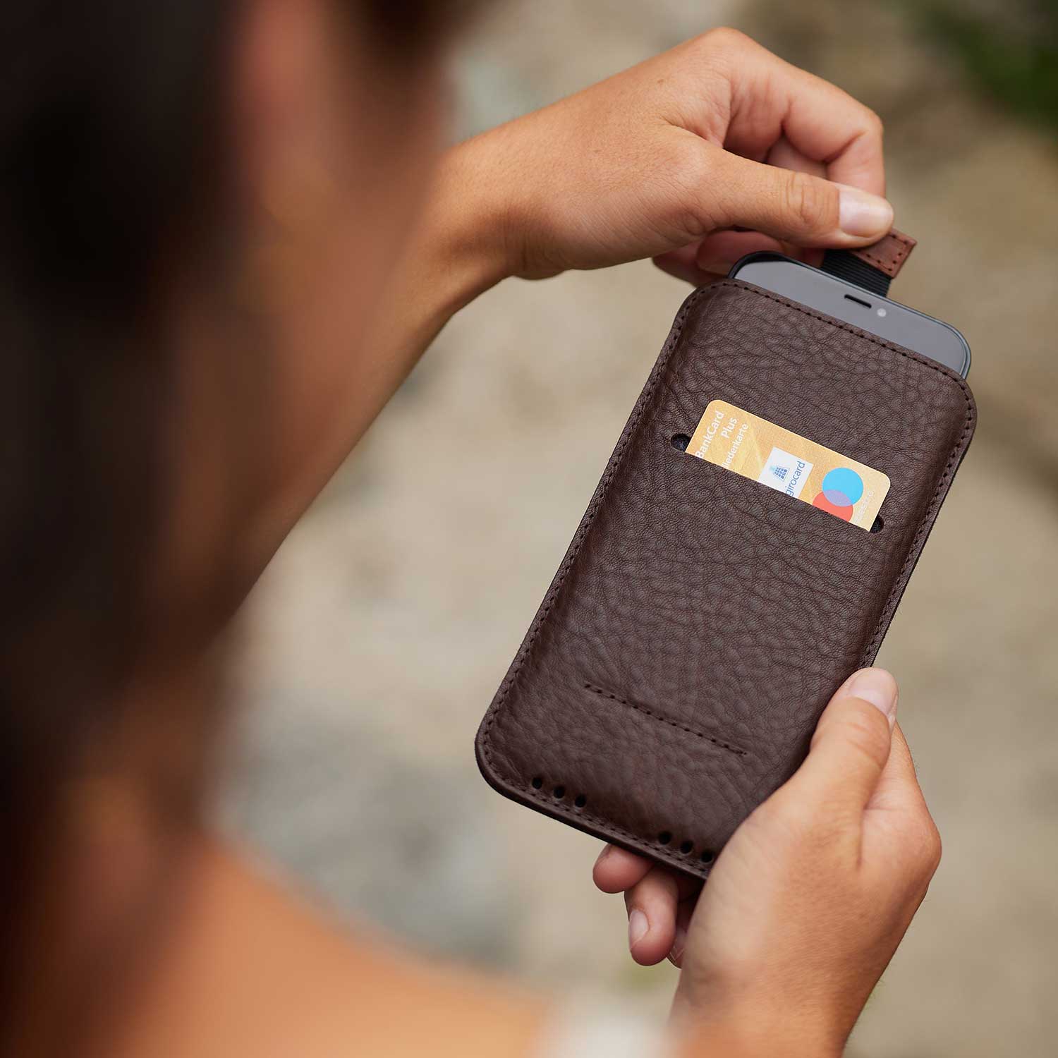 iPhone Leder Sleeve in Chocolate Braun von Good Wilhelm in der Hand – Elegante pflanzlich gegerbte iPhone Hülle mit praktischer Ziehhilfe für einfaches Herausziehen des Smartphones.