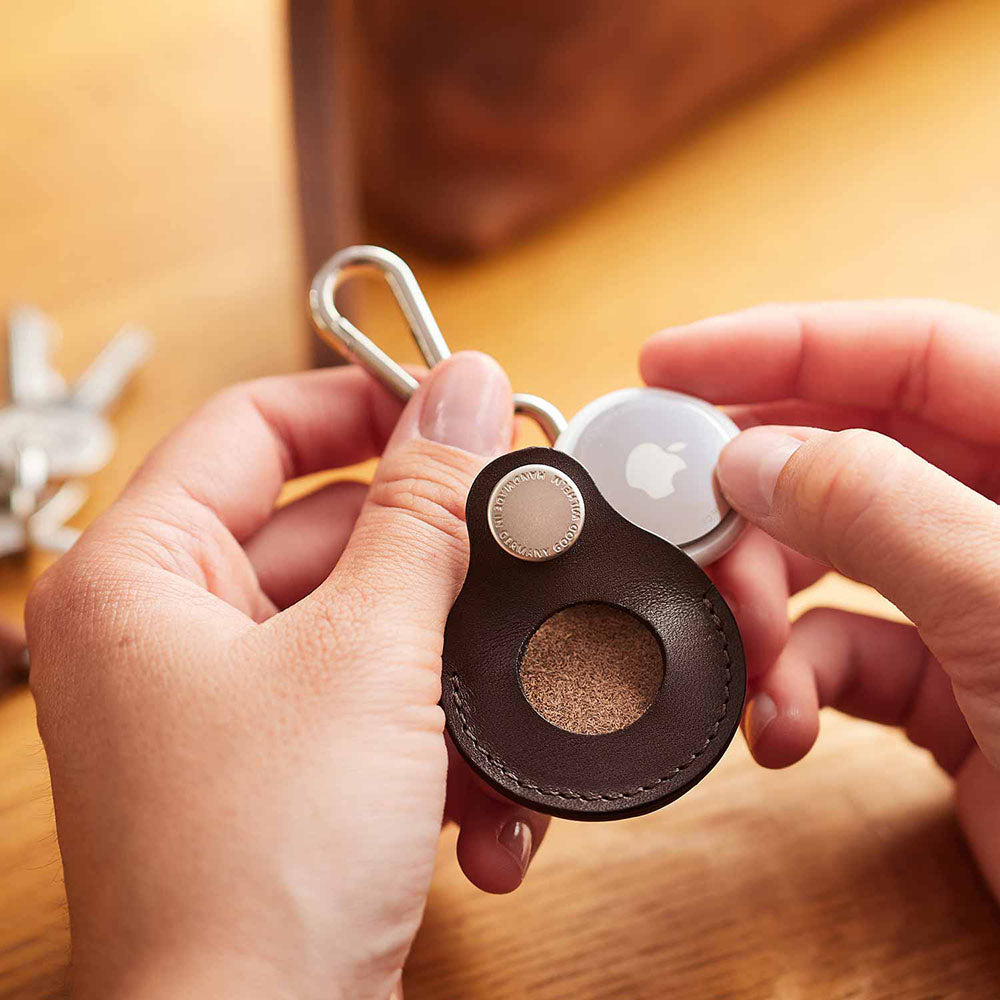 Zwei Hände sind gerade dabei einen Airtag von Apple in eine Airtaghülle zu schieben