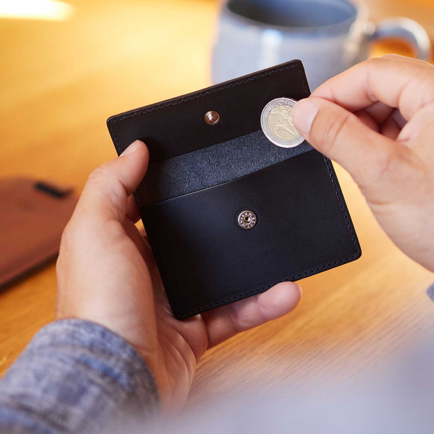 Ein Mann steckt eine Münze in das Münzfach der Geldbörse OTTO in der Farbe Schwarz von Goodwilhelm