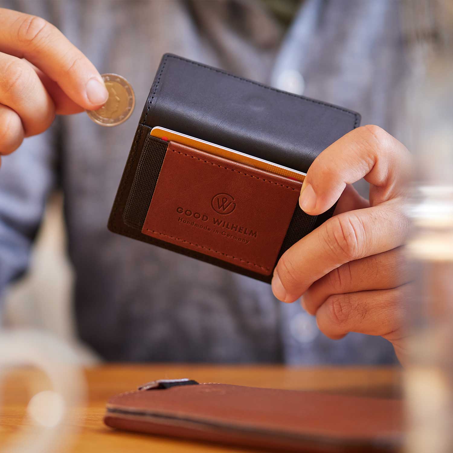 Ein Mann sitz an einem Tisch und steckt eine Münze in ein Portemonee von Goodwilhelm