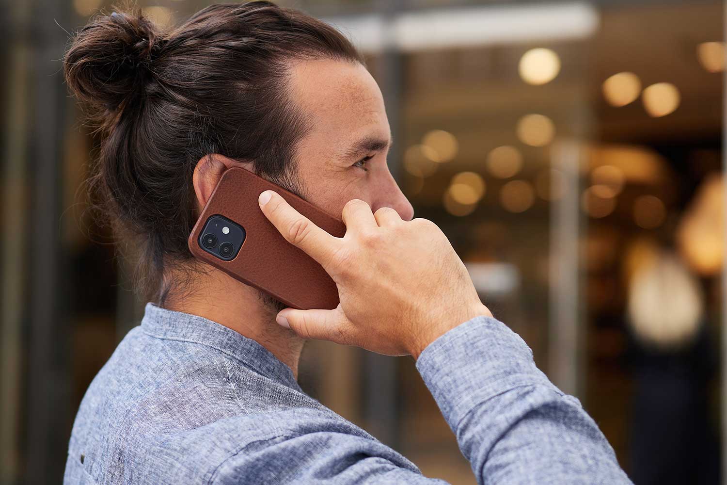 Ein Mann hält sich sein iPhone 13 Pro Max mmit Lederhülle an das Ohr und telefoniert
