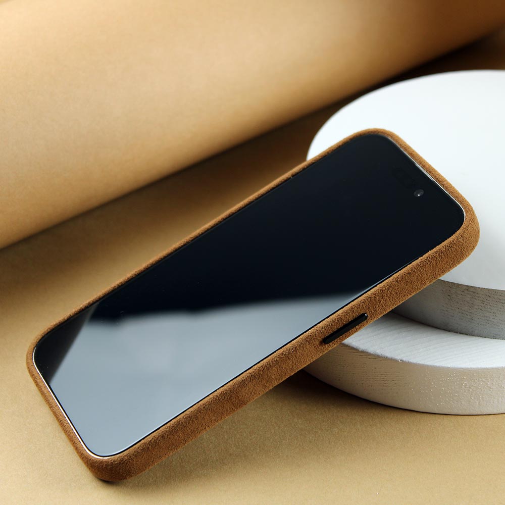 Auf eibem Tisch liegt eine Sandbraune Alcantara Hülle für das iPhone 15 Pro