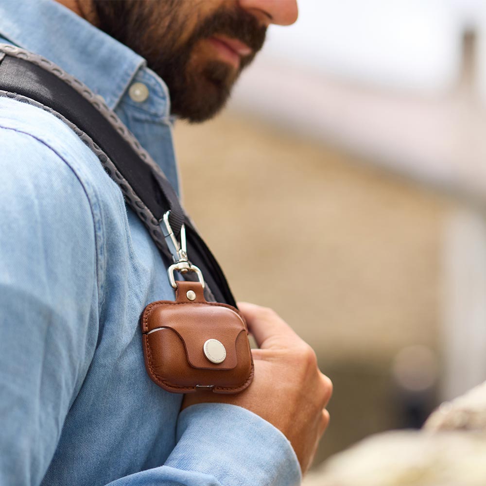 Eine Airpods Pro Hülle aus Leder hängt mit einem Karabinerhaken an einem Rucksack