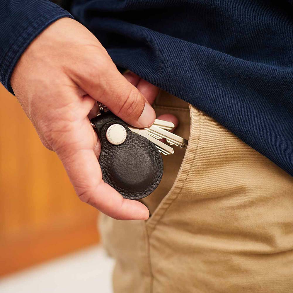 Eine Hand steckt gerade einen Schlüsselanhänger aus schwarzem Leder in die Hosentasche