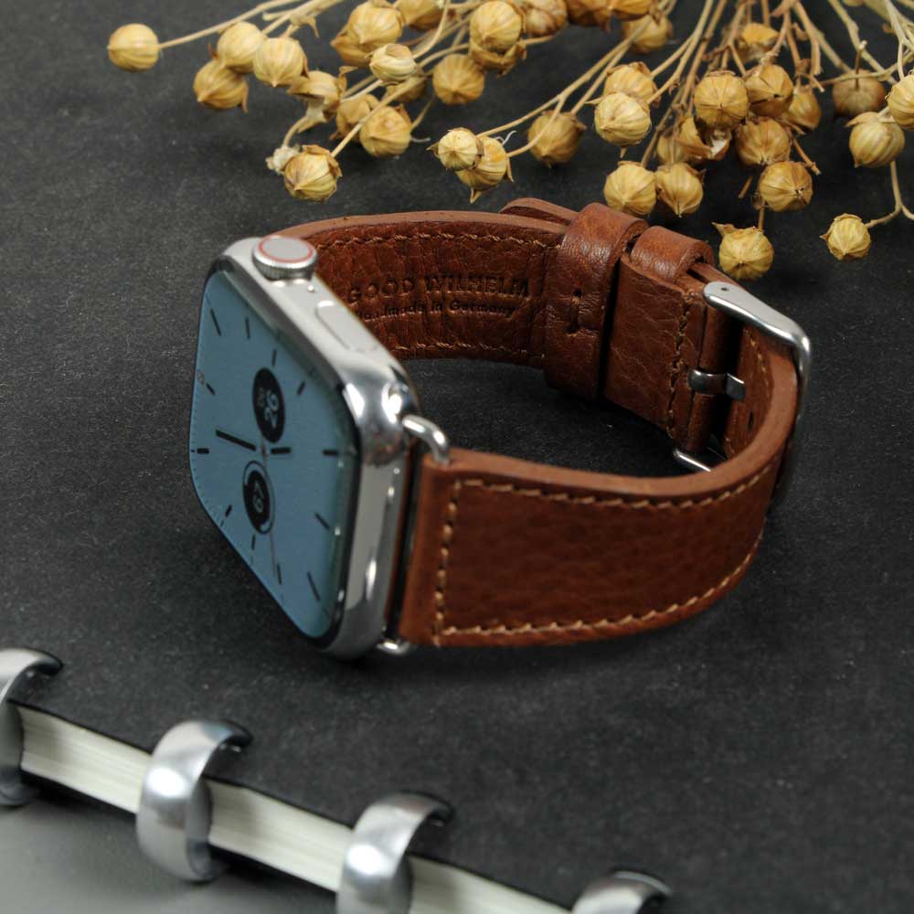 Auf einem Tisch liegt eine Apple Watch mit Lederarmband in der Farbe Cognac