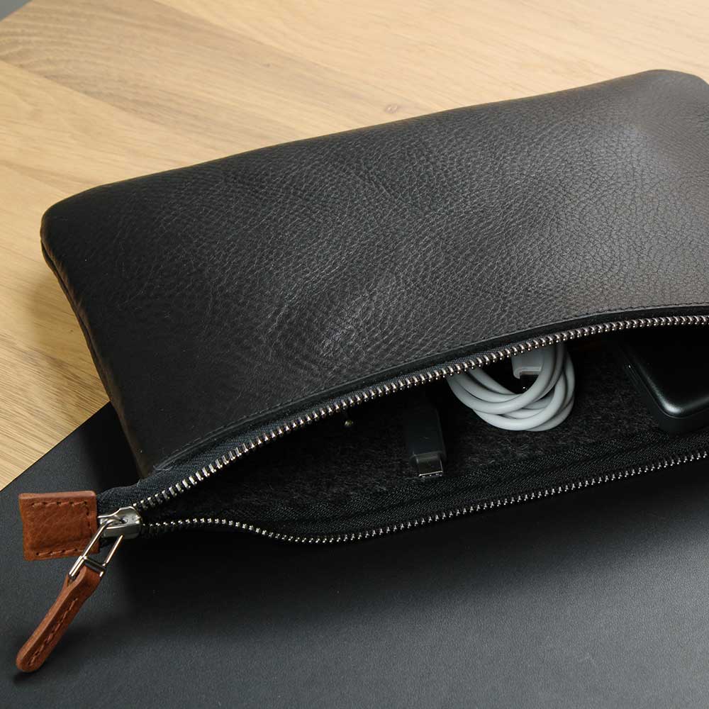 Auf einem Tisch liegt eine Tasche aus Leder für Kabel, Maus und Power Adapter