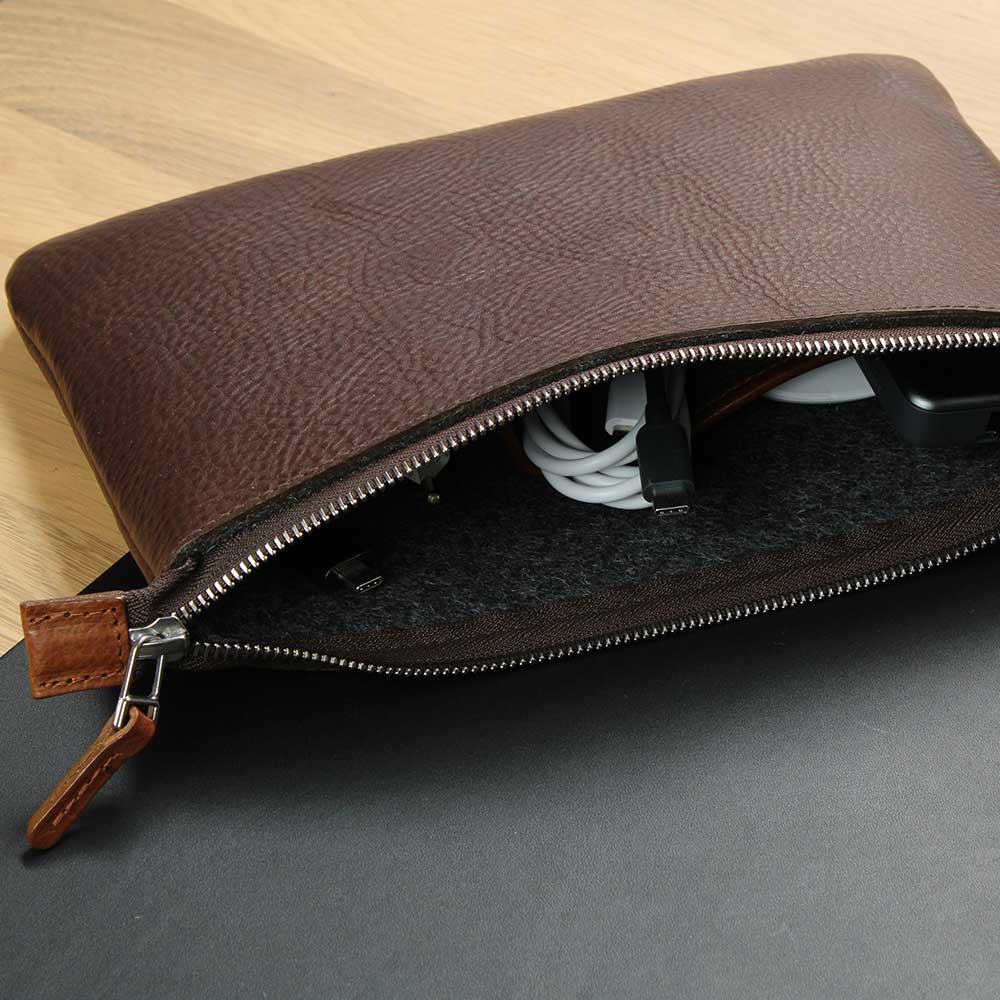 Auf einem Schreibtisch liegt eine offene Tasche aus Leder in denen Kabel und Maus untergebracht sind