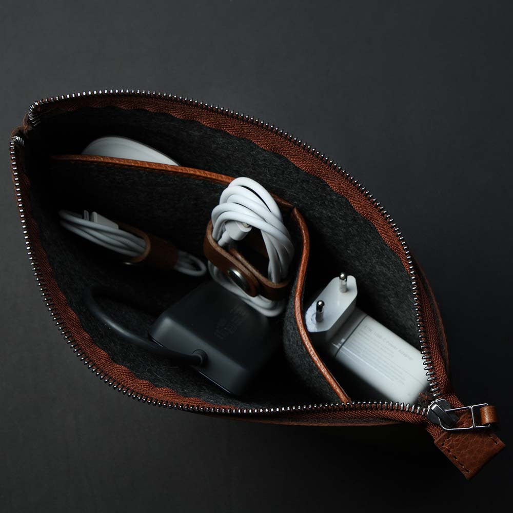 Auf einem Tisch steht eine offene Tasche aus Leder aus denen Kabel und eine Computer Maus herausschauen