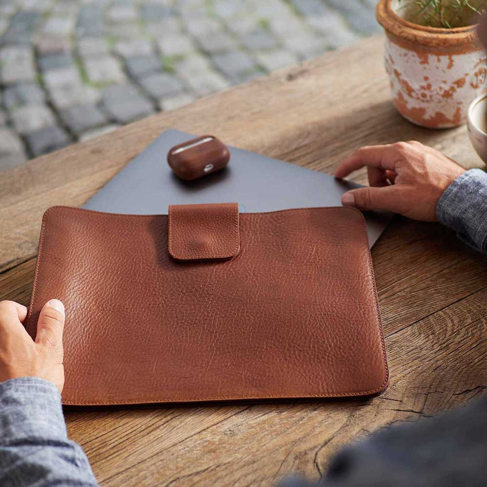 MacBook Hülle LUDWIG in der Farbe cognac von Goodwilhelm liegt auf Holztisch