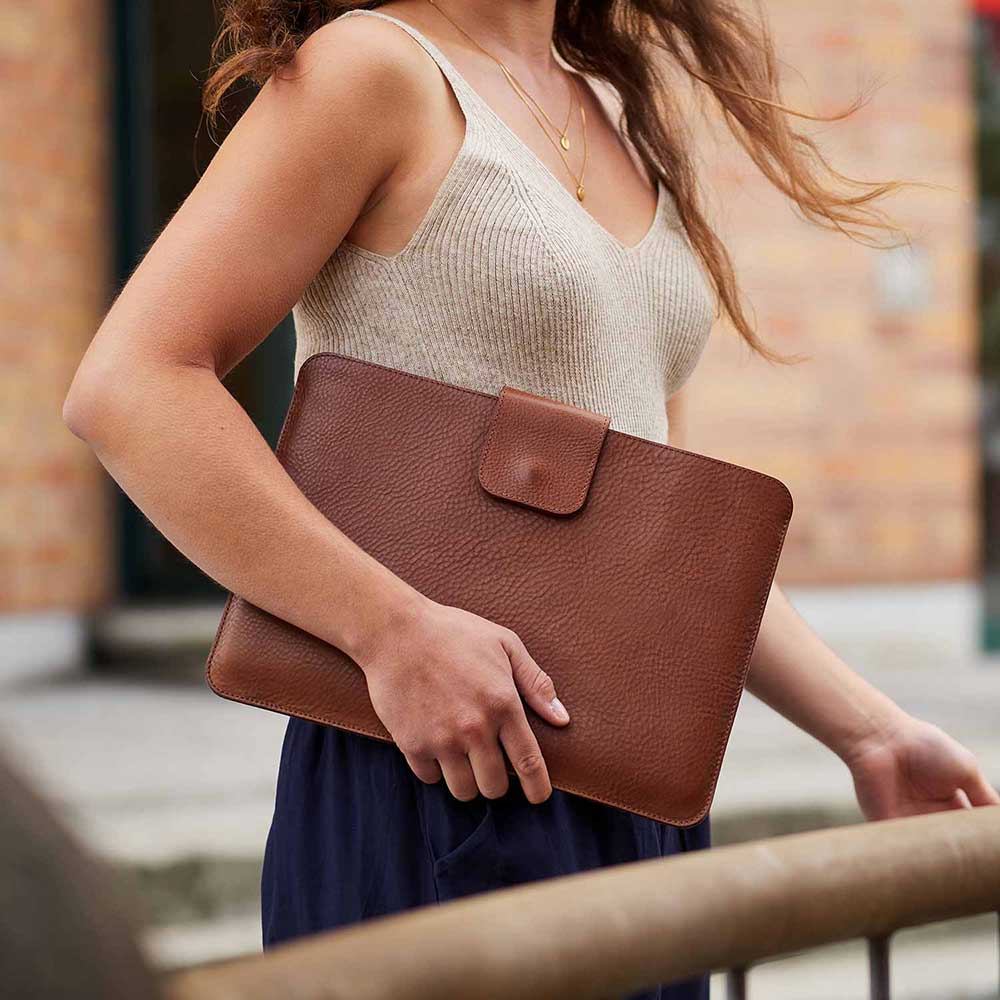 Frau hält MacBook Hülle LUDWIG von Goodwilhelm in der Farbe cognac fest