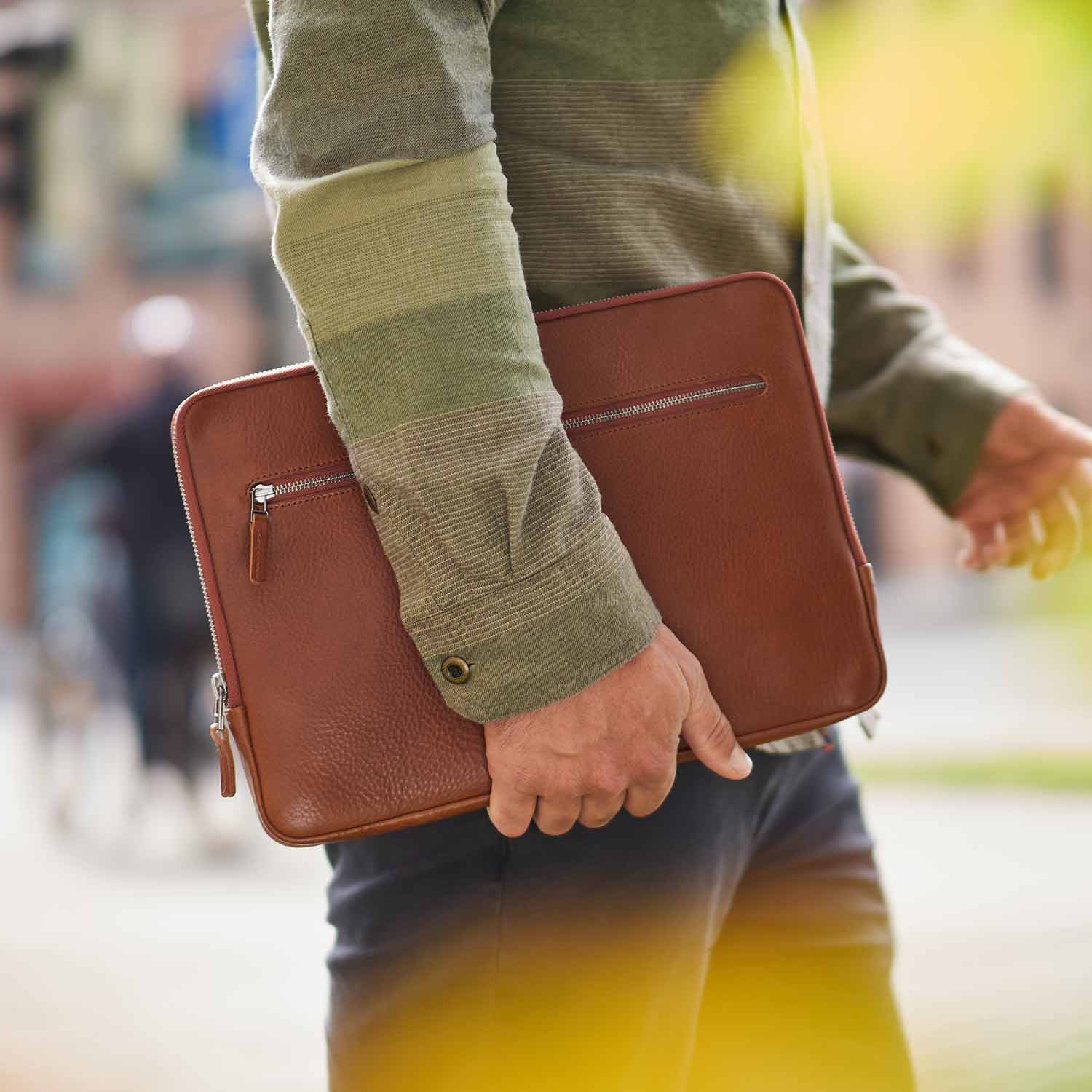 Ein Mann trägt eine Surface Laptop Hülle aus Leder unter dem Arm